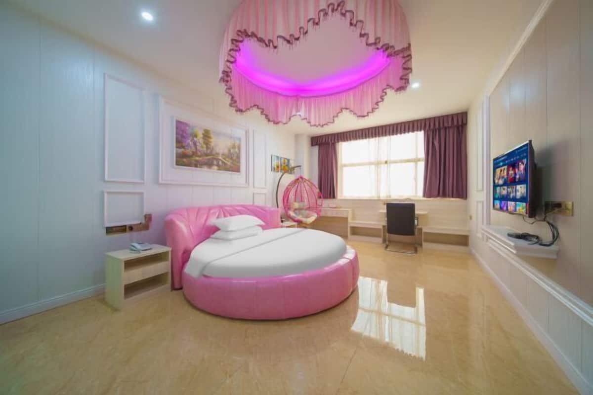 A bedroom with a round bed, a television, and a desk.