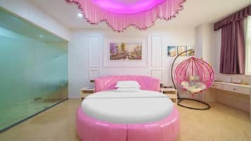 Un dormitorio con un pouf rosa, una silla colgante y una cama con cabecero blanco.