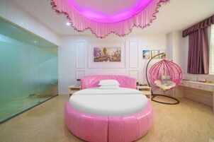 Un dormitorio con un pouf rosa, una silla colgante y una cama con cabecero blanco.