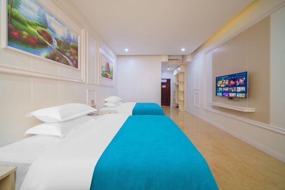 A hotel room with two beds, a TV on the wall, and artwork on the walls.