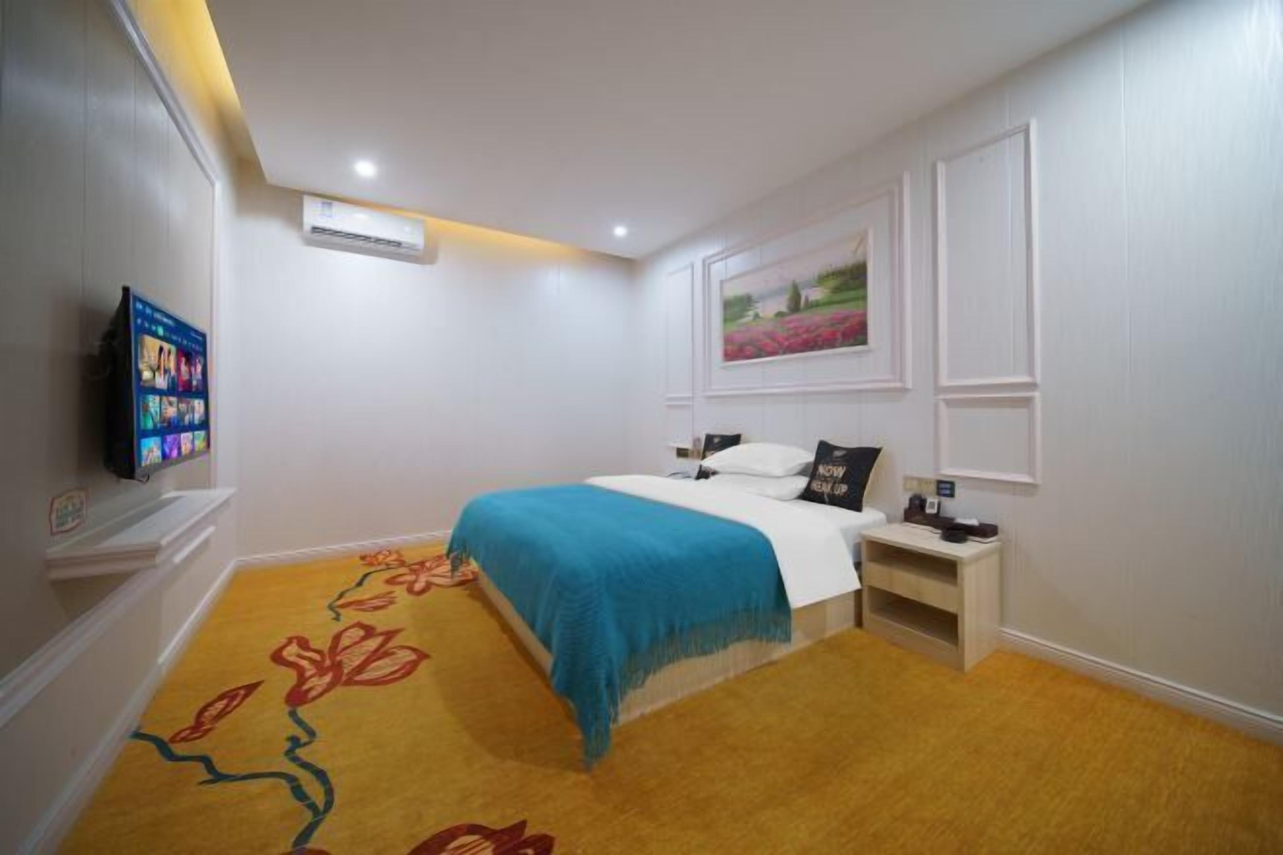 A bedroom with a bed, a TV, a nightstand, a painting, and a carpet with a floral pattern.