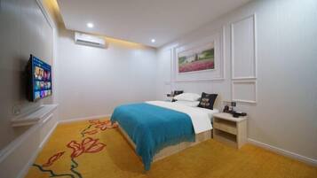 A bedroom with a bed, a TV, a nightstand, a painting, and a carpet with a floral pattern.