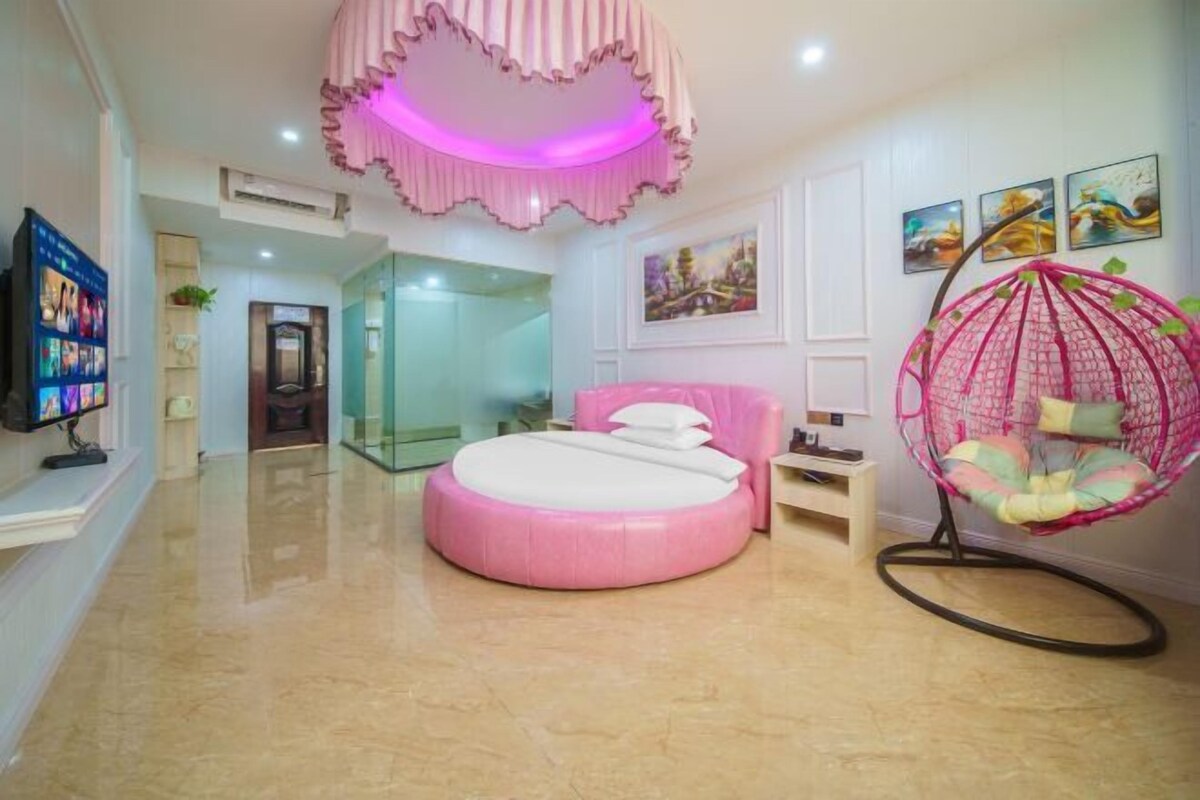 A bedroom with a round bed, a hanging chair, and a television on the wall.
