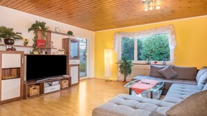 Een woonkamer met een televisie, bank en een raam met uitzicht op groen.