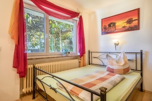 Ein Schlafzimmer mit einem Bett, einem Vorhangfenster, einem Heizkörper und einem Bild an der Wand.
