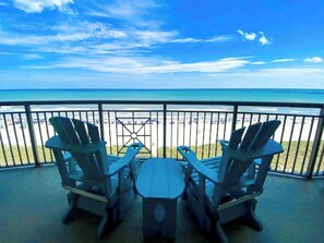 A balcony with two Adirondack chairs and a small table, overlooking a beach with a clear view of the ocean. - Mar Vista Grande 711 Oceanfront 3 BR 3 BA Condo (North Myrtle Beach)