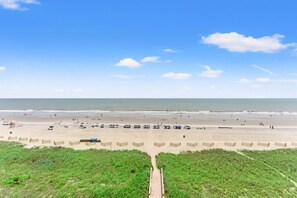 En strand med en træpromenade der fører til vandkanten, sandstrand og en klar himmel.