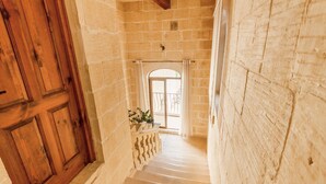 Eine Treppe mit Steinwänden und Holztüren führt zu einem Balkon mit Geländer und Topfpflanzen.