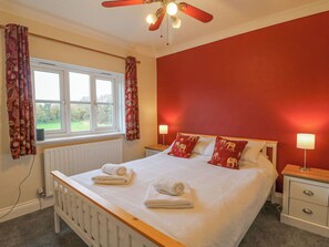 A bedroom with a bed, two bedside tables, a window with curtains, a radiator, and a ceiling fan. - Knapp Cottage (Weymouth)