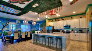 A modern kitchen with white cabinets, a central island with bar stools, and a ceiling with a green artificial grass design. - Bowling, Safari-themed, Private Pool, 1GB WiFi, video wall TV, sleeps 40 (Kissimmee)