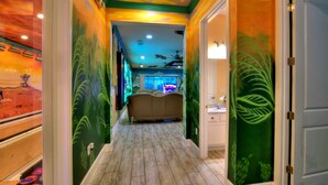 A hallway with a wooden floor, green walls with leaf patterns, a ceiling fan, and a bed in the distance. - Bowling, Safari-themed, Private Pool, 1GB WiFi, video wall TV, sleeps 40 (Kissimmee)
