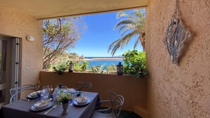 A dining area with a table set for two, overlooking a coastal view with palm trees and a clear blue sky. - Grecalotto Apartment (La Maddalena)