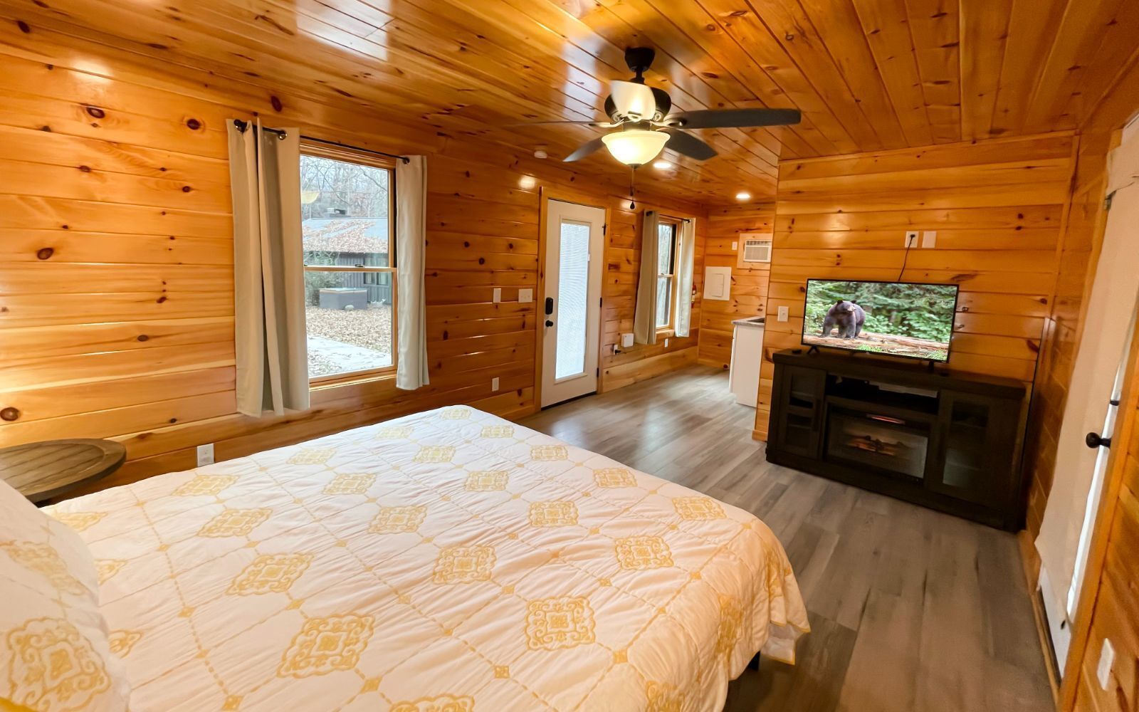 Ein Zimmer in einer Holzhütte mit einem Bett, einem Fernseher und einem Deckenventilator.