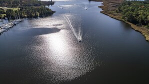 A marina with boats docked and a wake surfer creating a trail in the water. - Beautiful New 1 Bedroom Condo (New Bern)