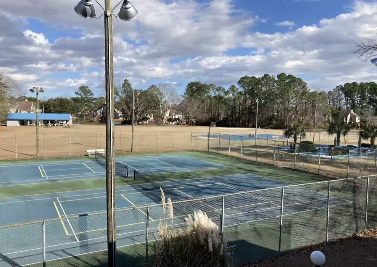 A tennis court with a fence, surrounded by trees and buildings.