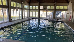 An indoor swimming pool with clear water, surrounded by large windows and a wooden ceiling. - Beautiful New 1 Bedroom Condo (New Bern)