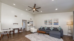A modern living room with a grey sofa, white coffee table, and a ceiling fan. - Beautiful New 1 Bedroom Condo (New Bern)