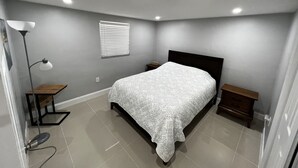Une chambre à coucher comprenant un lit, des tables de chevet, une lampe sur pied et une fenêtre avec des stores.