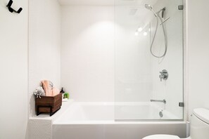 Un baño moderno con ducha envuelta en vidrio, una bañera blanca y un banco de madera con toallas.