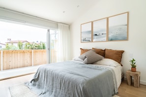 Une chambre avec une grande fenêtre, un lit avec une literie grise et un plancher en bois.