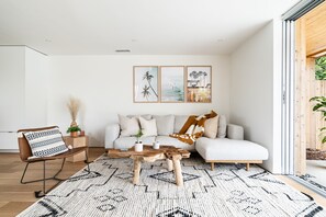 Un salon moderne avec un canapé, une table basse et un fauteuil. Des tableaux encadrés ornent le mur, et une plante est posée sur la table d’appoint.