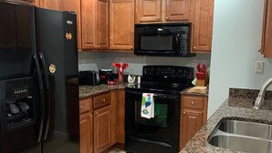 Una cucina con pensili e basi in legno, un frigorifero nero, un forno a microonde, un forno e un piano di lavoro in granito, oltre a un lavello in acciaio inossidabile.