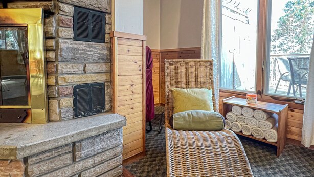 A cozy room with a stone fireplace, wicker furniture, and a view of the outdoors. - Ahmic Lake Resort's 2-Bedroom Cottage with Hot Tub (Gray Wolf Cottage) (Magnetawan)