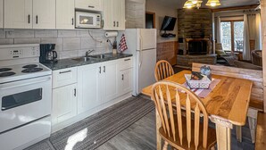 A modern kitchen with white cabinets, a microwave, stove, and a dining area with a wooden table and chairs. - Ahmic Lake Resort's 2-Bedroom Cottage with Hot Tub (Gray Wolf Cottage) (Magnetawan)