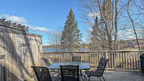A wooden deck with a table and chairs, surrounded by trees and a wooden fence. - Ahmic Lake Resort's 2-Bedroom Cottage with Hot Tub (Gray Wolf Cottage) (Magnetawan)