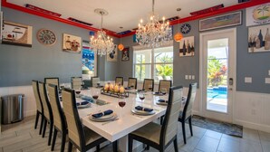 A dining area with a white table set for eight, surrounded by chairs, with chandeliers and wall art.