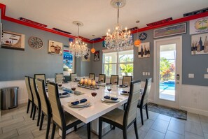A dining room with a white table set for six, surrounded by chairs, with chandeliers and wall art.
