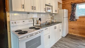 A modern kitchen with white cabinets, a built-in microwave, a stove, and a refrigerator. - Ahmic Lake Resort's 3-Bedroom Cottage (Red Fox Cottage) (Magnetawan)