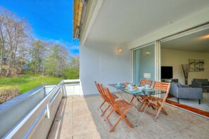 Ein Balkon mit Glastisch und Stühlen, eine Couch und ein Fernseher im angrenzenden Raum.