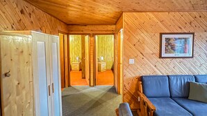 En stuga med träpanel på insidan, inredd med en soffa, en bänk, en garderob och en inramad tavla på väggen.