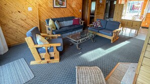 Interior acogedor de una cabaña con paredes y techos de madera, un conjunto de sofás, una mesa de centro y un sillón de mimbre.