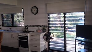A modern kitchen with a gas stove, oven, and sink, a clock on the wall, and a large window with a view of a parking area.