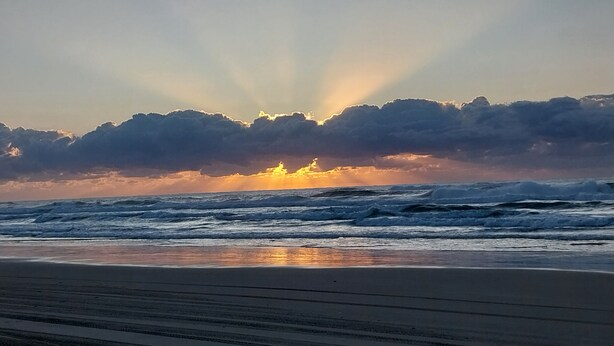 A beach with waves and a sunset.