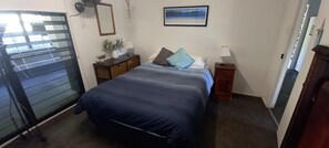 A bedroom with a bed, bedside tables, a nightstand, a mirror, a wall-mounted picture, and a window with blinds.