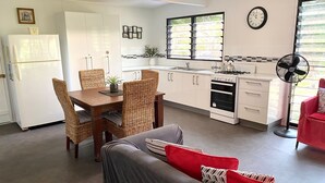 A compact kitchen with white cabinets, a dining table with wicker chairs, a gas stove, and a fan.