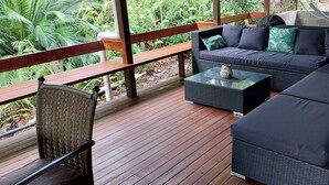 A covered outdoor seating area with a wooden deck, wicker furniture, and a hammock.