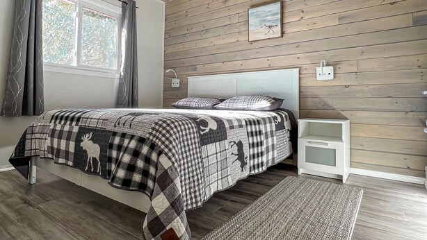 Un dormitorio con techo de madera, una cama con colcha a cuadros, una mesita de noche y una ventana con cortinas.