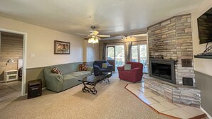 Una sala de estar con chimenea de piedra, un sofá, un sillón rojo y un ventilador de techo.