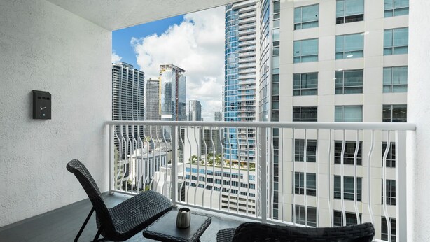 A balcony with wicker furniture, a small table, and a view of modern high-rise buildings. - Lovely Brickell Oceanview Studio (Miami)