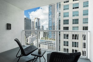 A balcony with wicker furniture, a small table, and a view of modern high-rise buildings. - Lovely Brickell Oceanview Studio (Miami)