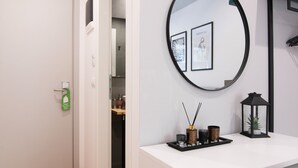A hotel room with a white desk, a round mirror, framed pictures, a black lantern, and a wooden floor. - Olvia Suites (Athens)