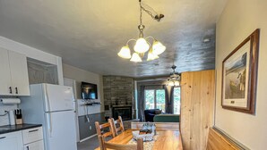 Eine moderne Küche mit weißen Schränken, einem eingebauten Kühlschrank, einem Holzespeisetisch mit Stühlen und einem Kamin aus Stein.