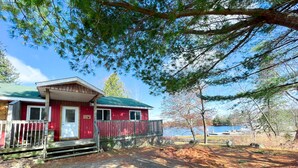 Eine rote Holzhütte mit einer Holzterrasse und einem Steg, der in einen See führt.