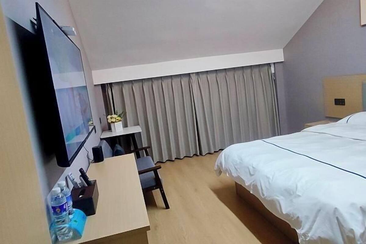 A hotel room with a bed, a desk with a chair, a television, and a window with curtains.