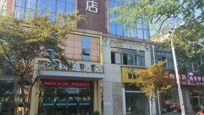 A hotel with a prominent sign, a storefront with a digital display, and a tree in the foreground. - Xuancheng Guangde Wanjia Express Inn (Guangde)