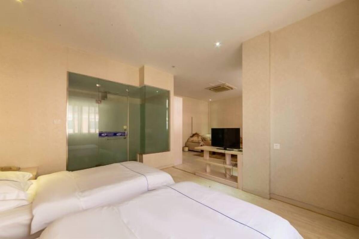 A hotel room with two beds, a television, and a glass partition.